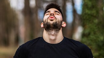 Man breathing in forest with head back and eyes closed